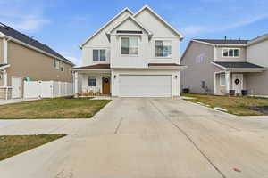 Traditional home with board and batten siding, driveway, an attached garage, covered porch, and a gate