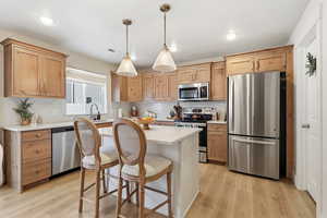 Kitchen featuring stainless steel appliances, a breakfast bar area, light countertops, decorative light fixtures, and light wood-style flooring