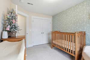 Bedroom featuring a nursery area, light carpet, a closet, and wallpapered walls