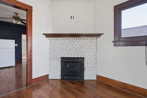 Detailed view of freestanding refrigerator, a ceiling fan, wood finished floors, and a fireplace