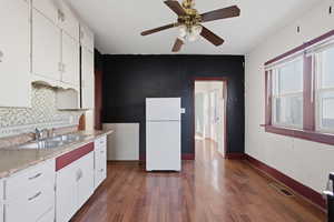 Kitchen with light countertops, freestanding refrigerator, white cabinets, and dark wood-style flooring