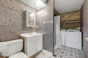 Full bathroom featuring brick wall, a shower with shower curtain, vanity, independent washer and dryer, and light flooring