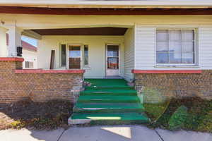 View of exterior entry featuring covered porch and brick siding