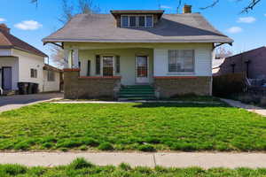 Bungalow featuring brick siding, covered porch, a front lawn, a chimney, and roof with shingles