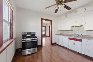 Kitchen featuring stainless steel gas range, white cabinets, light countertops, and dark wood-style flooring