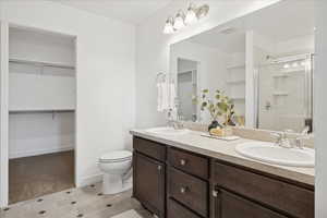 Bathroom with a spacious closet, double vanity, a stall shower, and light flooring