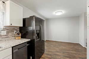 Kitchen featuring dishwashing machine, backsplash, dark wood-style floors, white cabinets, and light stone countertops