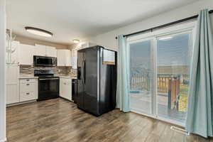 Kitchen with black appliances, white cabinetry, tasteful backsplash, and dark wood-type flooring