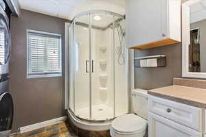 Bathroom with a shower stall, stacked washing machine and dryer, a drop ceiling, stone tile flooring, and vanity