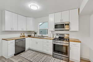 Kitchen featuring wooden counters, stainless steel appliances, white cabinetry, light wood-type flooring, and a textured ceiling