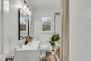 Full bath with a textured wall, vanity, a shower with shower curtain, and light wood-style floors