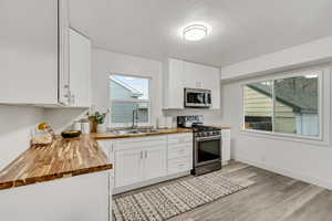 Kitchen featuring wooden counters, white cabinets, appliances with stainless steel finishes, and light wood finished floors