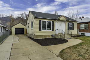 Bungalow featuring an outbuilding, concrete driveway, a detached garage, and roof with shingles