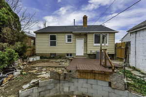 Back of house with a chimney, a deck, and a shingled roof