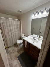 Bathroom with vanity, curtained shower, a textured ceiling, and stone finish flooring