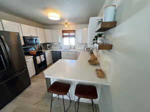 Kitchen with black appliances, open shelves, white cabinets, a kitchen breakfast bar, and a peninsula