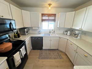 Kitchen featuring black appliances, white cabinetry, and light wood-style flooring