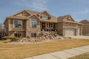 View of front of home with stone siding, covered porch, an attached garage, and concrete driveway