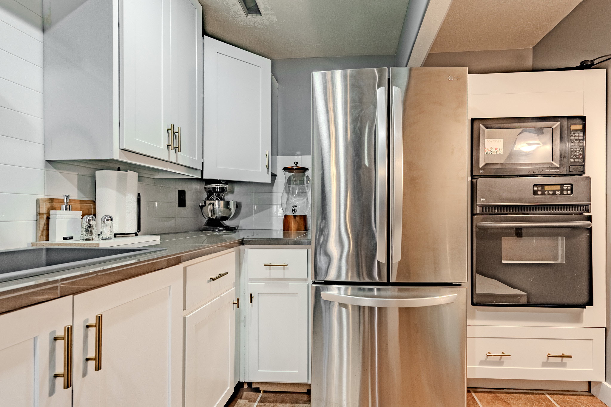 Kitchen featuring black appliances, white cabinetry, tasteful backsplash, and tile countertops