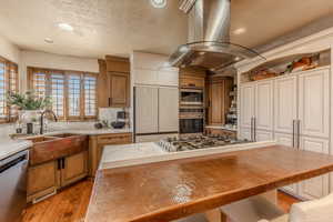 Kitchen with island exhaust hood, appliances with stainless steel finishes, a kitchen island, recessed lighting, and brown cabinets