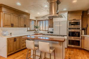 Kitchen with stainless steel appliances, island range hood, wood counters, brown cabinetry, and a kitchen island