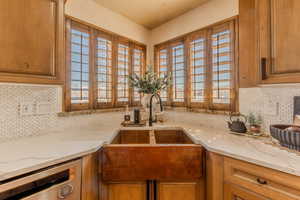 Kitchen featuring decorative backsplash, light stone countertops, and brown cabinetry