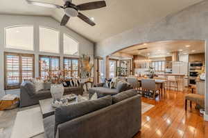 Living area with vaulted ceiling, arched walkways, light wood-style flooring, a chandelier, and a ceiling fan