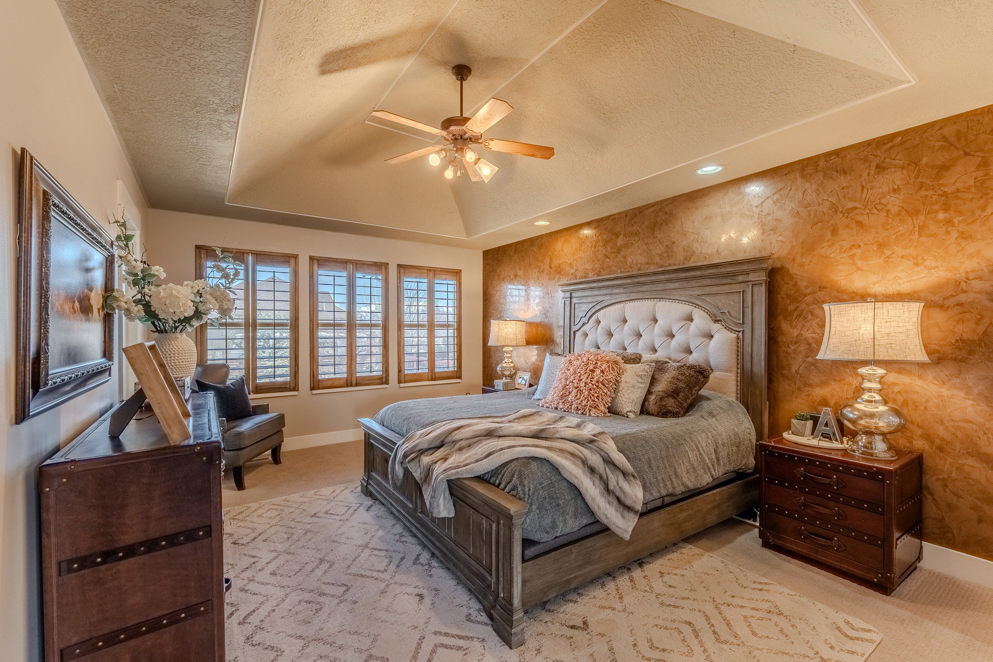 Bedroom featuring a raised ceiling, a textured ceiling, ceiling fan, an accent wall, and wallpapered walls