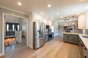 Kitchen featuring pendant lighting, gray cabinetry, stainless steel appliances, light stone counters, and white cabinets