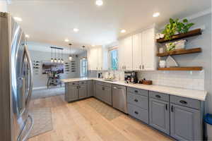 Kitchen featuring gray cabinetry, stainless steel appliances, a peninsula, white cabinetry, and pendant lighting