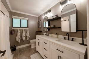 Bathroom with double vanity, crown molding, and a shower with curtain