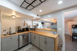 Kitchen with butcher block counters, gray cabinets, stainless steel appliances, a peninsula, and decorative backsplash