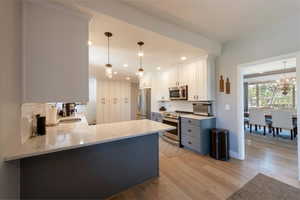 Kitchen with white cabinetry, light stone countertops, appliances with stainless steel finishes, a peninsula, and decorative light fixtures