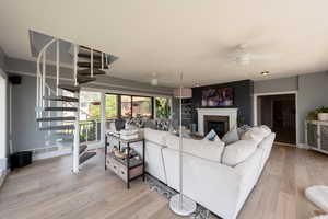 Living area featuring stairs, light wood-style flooring, a glass covered fireplace, and ceiling fan