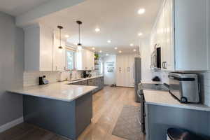 Kitchen featuring light stone counters, decorative backsplash, white cabinets, open shelves, and appliances with stainless steel finishes