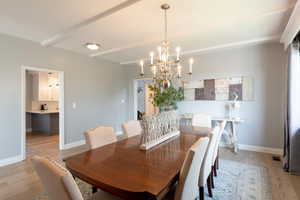 Dining area with light wood-style floors, beam ceiling, and a chandelier