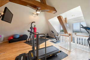 Workout area featuring light wood-style flooring, ceiling fan, and beam ceiling