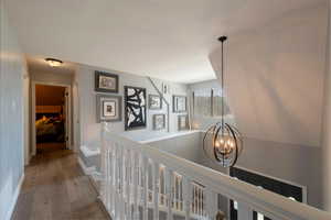 Hallway with light wood-type flooring, a chandelier, and an upstairs landing