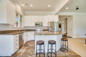 Kitchen featuring a kitchen bar, appliances with stainless steel finishes, a center island, white cabinets, and crown molding
