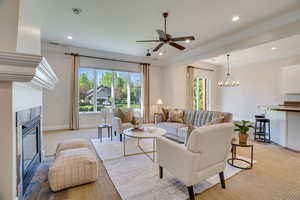 Living room with a chandelier, a tiled fireplace, ceiling fan, light carpet, and ornamental molding
