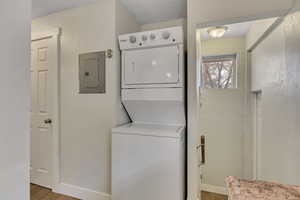 Laundry area featuring stacked washing machine and dryer, light wood finished floors, and electric panel