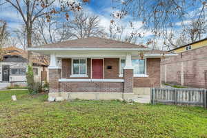 View of front facade with brick siding, covered porch, and a shingled roof