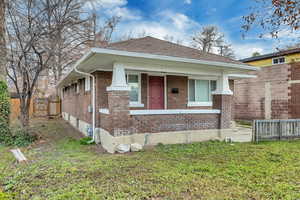 View of front of house with brick siding, a porch, a gate, and roof with shingles