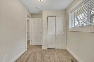Unfurnished bedroom with light colored carpet, a closet, and a textured ceiling