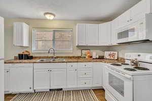 Kitchen with white appliances, white cabinetry, a textured ceiling, and dark countertops