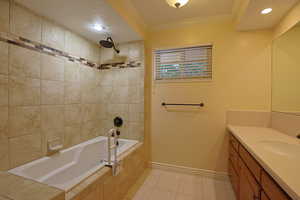 Full bathroom with ornamental molding, tiled shower / bath combo, vanity, light tile patterned flooring, and a textured ceiling
