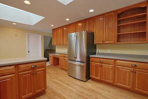 Kitchen with open shelves, a skylight, freestanding refrigerator, brown cabinets, and recessed lighting