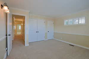 Unfurnished bedroom featuring light carpet, multiple windows, crown molding, and a closet