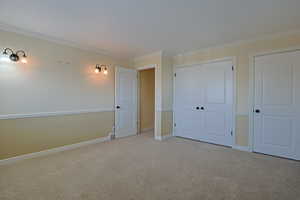 Unfurnished bedroom featuring carpet flooring, crown molding, and a closet