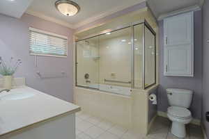 Full bath featuring vanity, light tile patterned floors, crown molding, and shower / bath combination with glass door